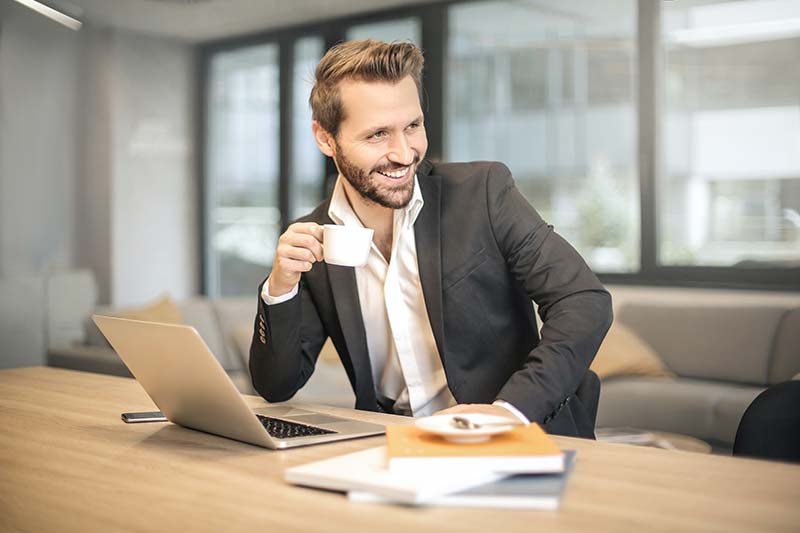 Collaborateur souriant buvant du café devant son ordinateur à Rennes